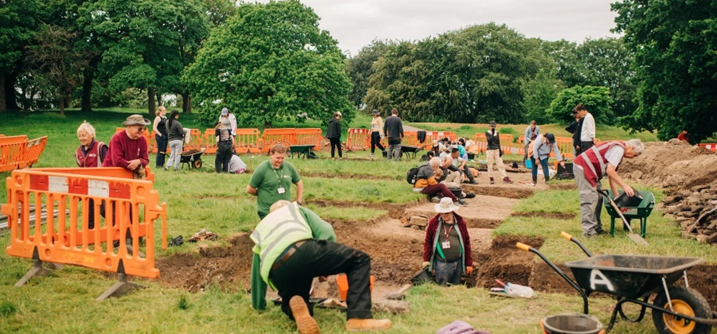 A view looking out over an archaeology dig with many people digging and surveying the ground.