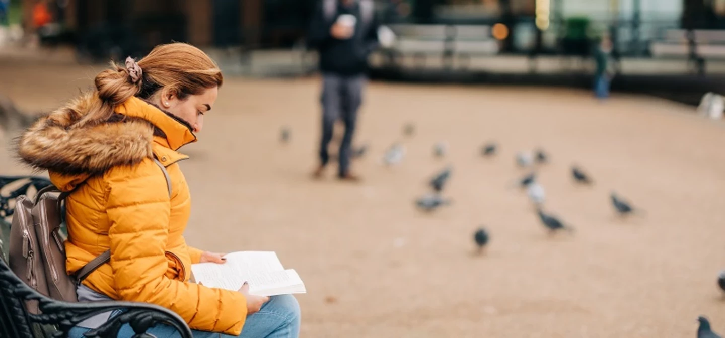 Woman reading a book on a park bench near the Serpentine Bar and kitchen