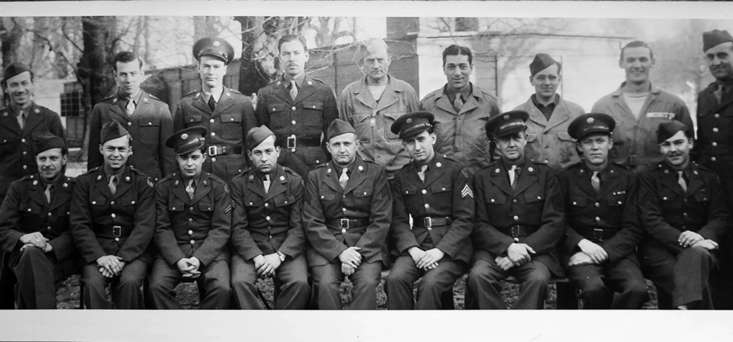 A black and white group image of Second World War United States airmen. Trees and huts in Bushy Park can be seen behind.