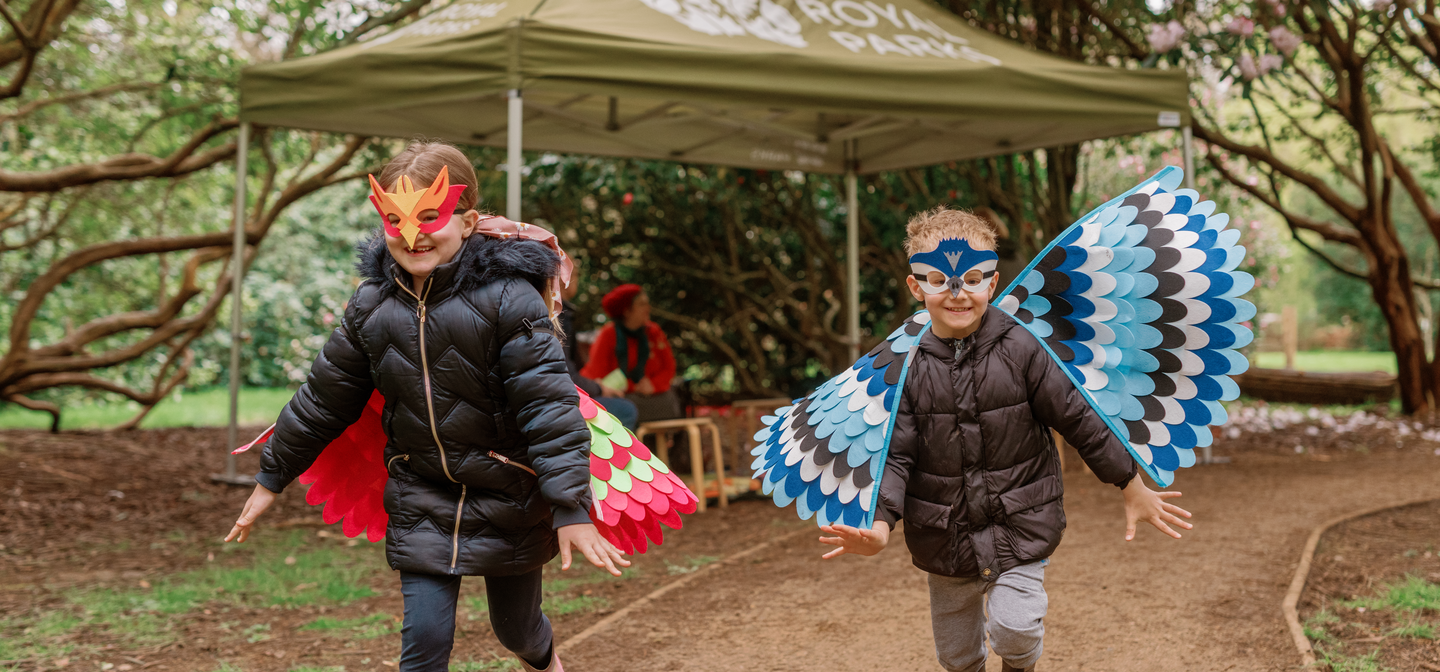 Two children running along a path wearing bird wing costumes