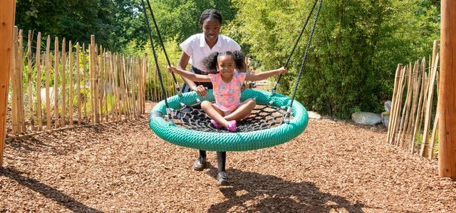 Parent and child on the big swing in Greenwich Playground in summer