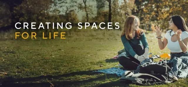 Two people sitting on grass on the right and the words Creating Spaces for Life on the left. 