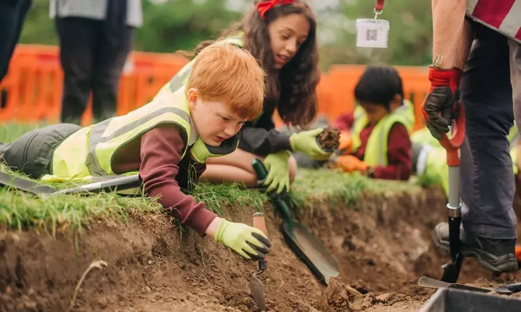 A child lies on the ground over the archaeology dig and looks for 