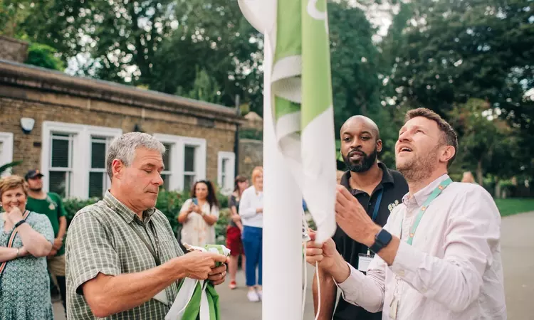 Several Royal Parks staff members hoisting a Green Flag in Brompton Cemetery