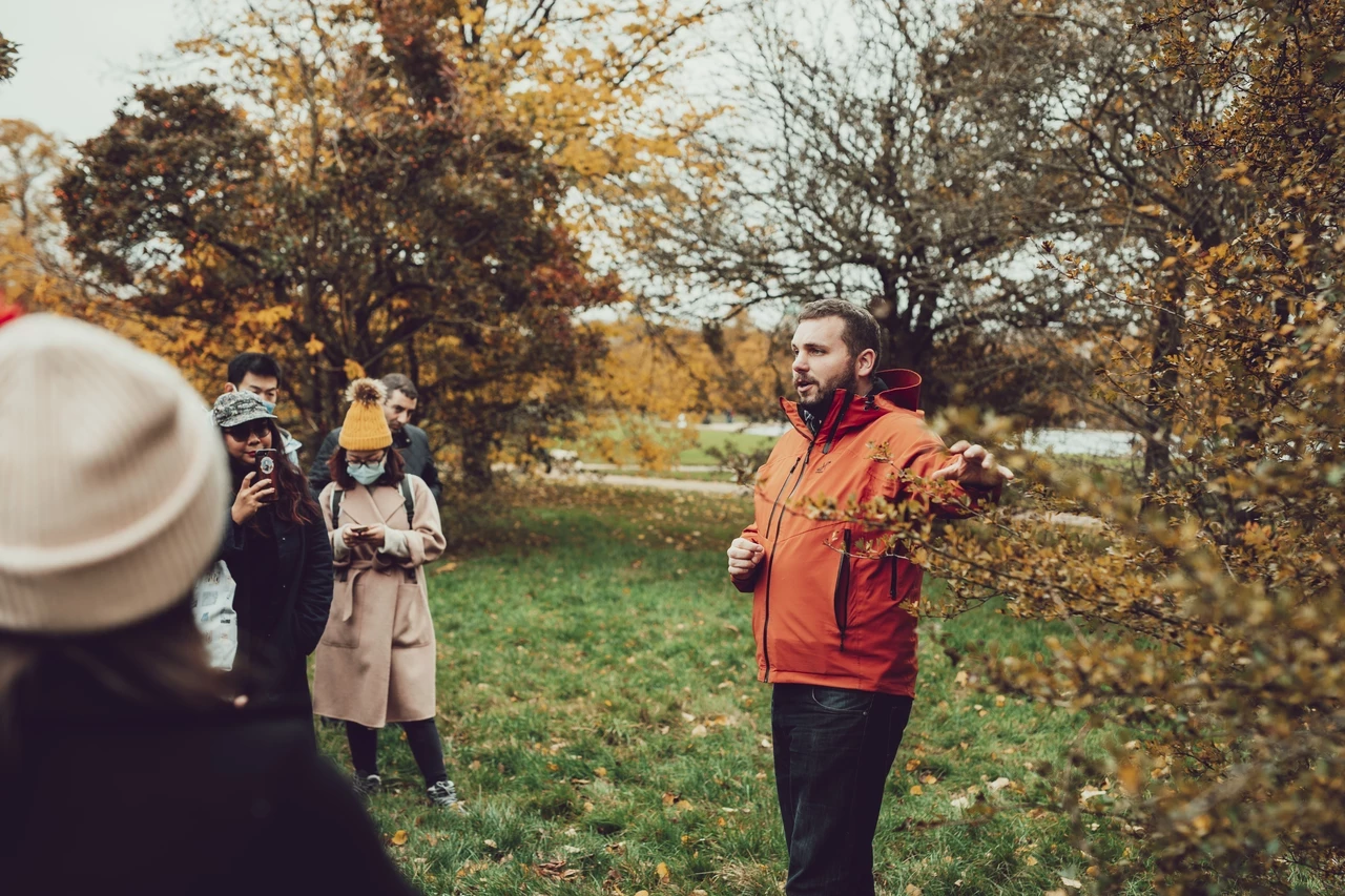 Image of a man in an orange jacket, guiding a tour in an outdoor setting.