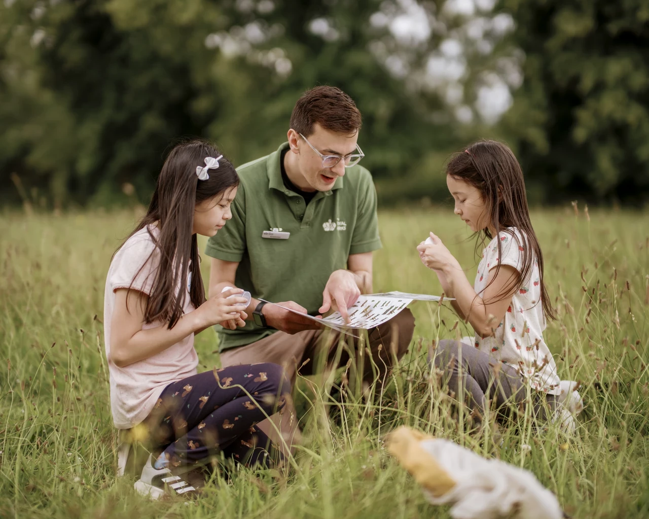 Image of a man explaining the content of a map or booklet, to two children in an outdoor setting.