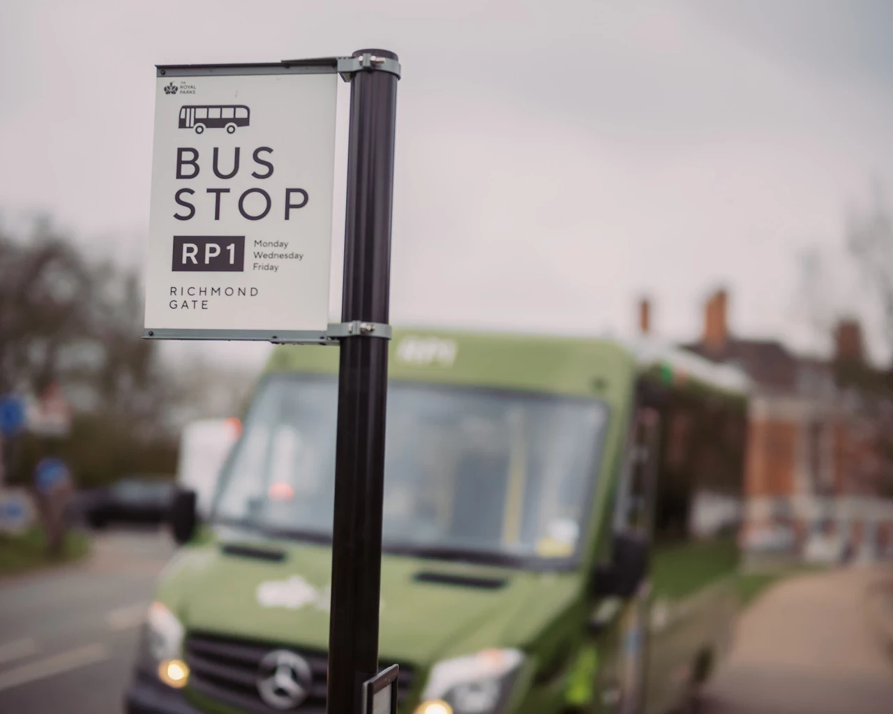 An image of a bus stop sign with an out of focus green minibus in the background